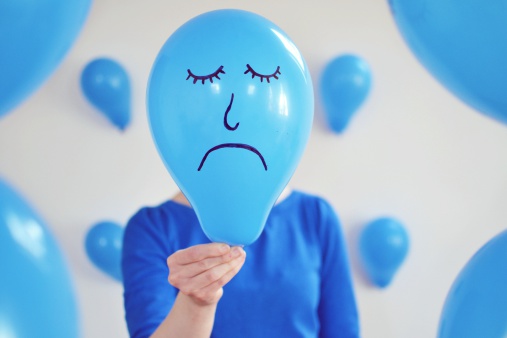 Woman holding sad blue balloon to her face